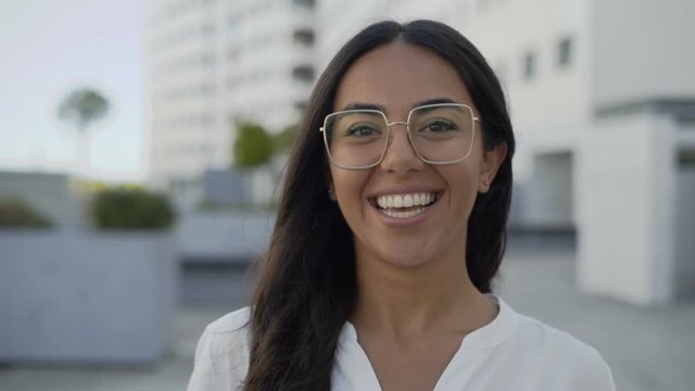 Smiling Latin businesswoman talking and looking at camera outdoors. Beautiful smiling manager in eyeglasses telling something in city. Conversation concept