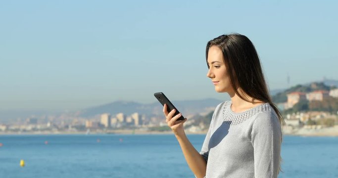 Side view of an excited woman reading good news on a smart phone on the beach