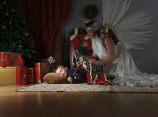 Obraz na płótnie Canvas Sleeping boy under the Christmas tree and guardian angel covering him with a blanket.