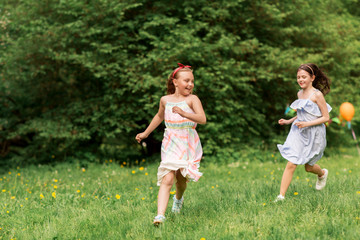 Obraz premium friendship, childhood, leisure and people concept - happy girls or friends playing tag game at birthday party in summer park