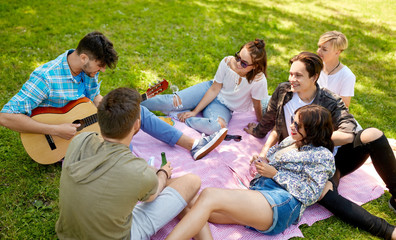 Fototapeta premium friendship, leisure and summer concept - group of happy smiling friends with guitar and non alcoholic drinks chilling on picnic blanket at summer park