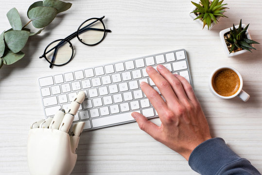 cropped image of business with prosthesis hand typing on computer keyboard at table in office