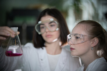 Chemical laboratory. Two young woman holding a flask with red liquid in it looking at it