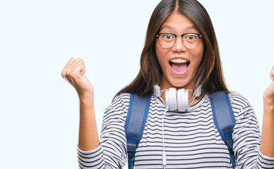 Young asian student woman wearing headphones and backpack over isolated background celebrating surprised and amazed for success with arms raised and open eyes. Winner concept.