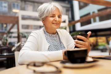 technology, old age and people concept - happy senior woman with smartphone at street cafe