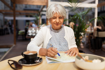 travel, tourism, retirement and people concept - happy senior woman with map and coffee at street cafe