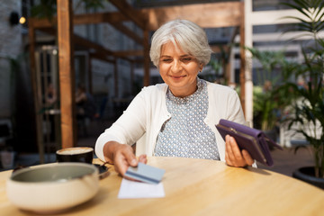 old age, leisure, payment and finances concept - happy senior woman with credit card and wallet paying bill for coffee and dessert at street cafe