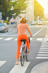 Girl in orange trousers and striped t-shirt on a bicycle in the city.