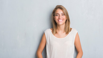 Beautiful young woman standing over grunge grey wall with a happy face standing and smiling with a confident smile showing teeth