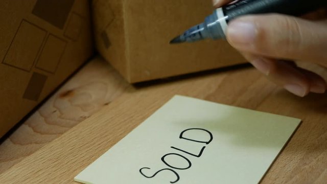 4K footage of woman hand writing word SOLD on notepad with black magic pen and stick memo note on delivery box