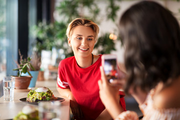 leisure, technology and people concept - female friends having lunch and photographing by smartphone at restaurant or cafe