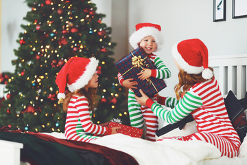 happy family mother and children in pajamas opening gifts on christmas morning near   tree