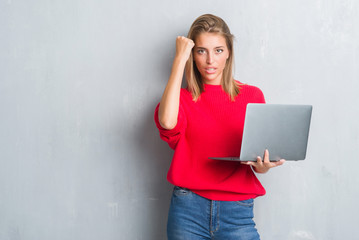Beautiful young woman over grunge grey wall using computer laptop annoyed and frustrated shouting with anger, crazy and yelling with raised hand, anger concept