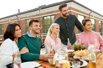 leisure and people concept - happy friends with drinks having barbecue party on rooftop