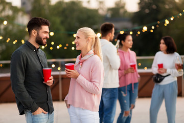 leisure, celebration and people concept - happy friends with drinks in party cups toasting at rooftop