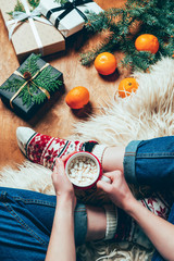 partial view of woman with cup of hot chocolate and marshmallow on background with christmas gifts and tangerines
