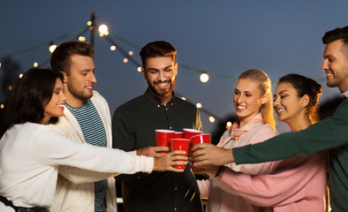 leisure, celebration and people concept - happy friends with drinks toasting at rooftop party at night