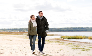 love, relationship and people concept - smiling couple walking along autumn beach and hugging