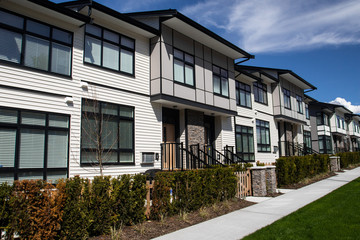 A street of family houses in suburban area with concrete side walk and asphalt road in front. Residential houses with cars parked on driveways in front.