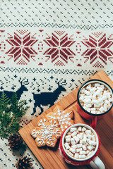top view of cups of hot chocolate with marshmallows and cookies on sweater backdrop, christmas breakfast concept