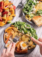 fried eggs and salad for breakfast, hands with cutlery, close-up