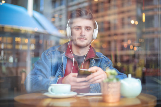 Handsome guy sitting in a bar, listening something with headphones