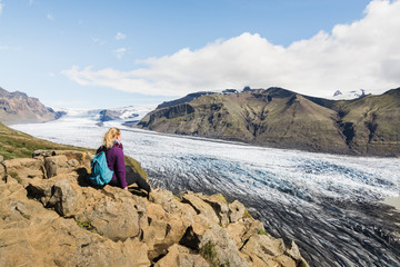 Woman sitting on rocks overlooking Skaftafellsjokull part of Vatnajokull glacier in Skaftafell...