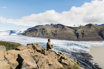 Man sitting on rocks overlooking Skaftafellsjokull part of Vatnajokull glacier in Skaftafell national park, Iceland