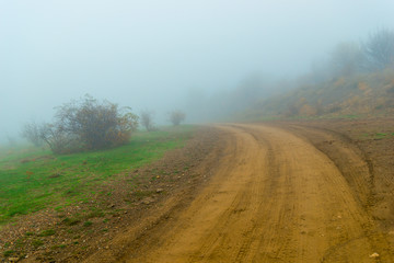 Fototapeta na wymiar Dirt road leading into thick fog. Autumn landscape on a foggy day
