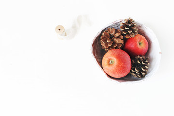 Red apple fruit and pine cones in ceramic bowl and silk ribbon on white table background. Christmas holiday styled stock photo. Winter food composition. Flat lay, top view.