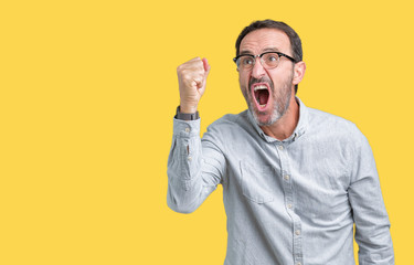 Handsome middle age elegant senior man wearing glasses over isolated background angry and mad raising fist frustrated and furious while shouting with anger. Rage and aggressive concept.
