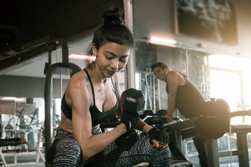 Asian woman lifting dumbbell at gym and man is peek her.