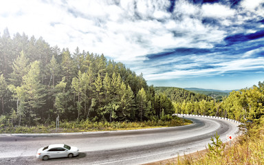 Scenic panorama scenery overview of taiga forest mountain road leading through green trees with white car on foreground beautiful sloppy hills background russia siberia nature travel tourism theme