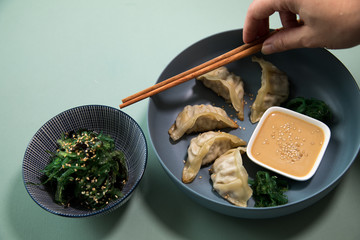Frau isst gebratene asiatische Dim Sum Teigtaschen mit Wakame Algen Salat und Sesam Soße auf...