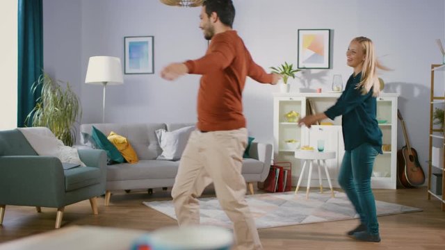 Beautiful Happy Young Couple Dancing in the Middle of the Living Room. Husband and Wife Cheerfully Dance at Home.