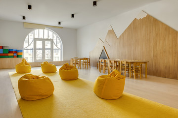 yellow bean bag chairs and wooden tables in kindergarten playing room - obrazy, fototapety, plakaty