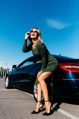 Fototapeta na wymiar Photo of happy sexy blonde woman in sunglasses in long dress standing near black car with open door