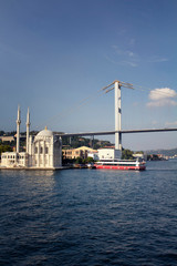 View of old, historical Ortakoy Mosque by Bosphorus, tour boat, bridge and European side of Istanbul.