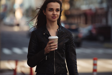 Beautiful woman holding paper coffee cup and enjoying a walk in the city