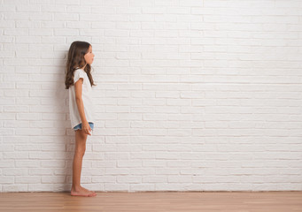 Young hispanic kid stading over white brick wall looking to side, relax profile pose with natural face with confident smile.