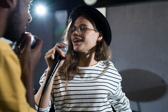 Waist up portrait of contemporary young woman singing to microphone during band rehearsal, copy space