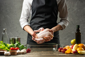 The chef holds a raw chicken in his hands against the background with vegetables, for a holiday, Christmas, New Year, Benefit Day. Background for the menu and for the book of cooking recipes