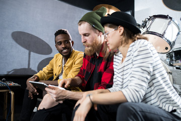 Portrait of three musicians using digital tablet while discussing songwriting in rehearsal studio