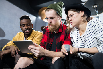 Low angle view at multi-ethnic group of  musicians using digital tablet while discussing songwriting in rehearsal studio - obrazy, fototapety, plakaty