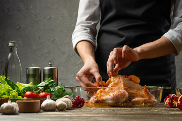 The chef prepares chicken with fruit for baking for a holiday, Christmas, New Year, on the background of a concrete wall. Background for the menu and for cooking recipes
