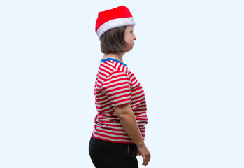 Young adult woman with down syndrome wearing christmas hat over isolated background looking to side, relax profile pose with natural face with confident smile.