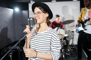 Waist up portrait of contemporary young woman smiling happily while singing on stage during band performance, copy space