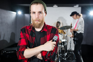 Portrait of contemporary bearded man holding microphone and looking at camera during band rehearsal in studio, copy space