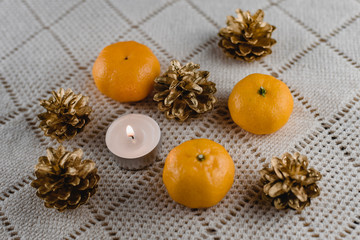 Christmas composition of mandarins , golden cones and a burning decorative candle on a light background
