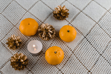 Christmas composition of mandarins , golden cones and a burning decorative candle on a light background